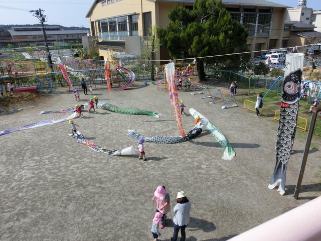 園児や職員が園庭の上に鯉のぼりをつないだロープを張り、泳がせる準備をしている写真