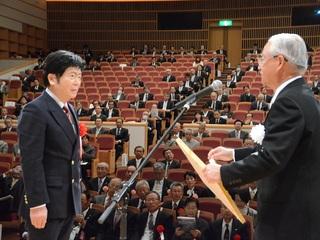 会場の舞台上で表彰される、森町ロゴマーク制作者の駒井瞭さんの写真