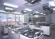 キッチン台が並ぶ白っぽく明るい室内の調理実習室の写真